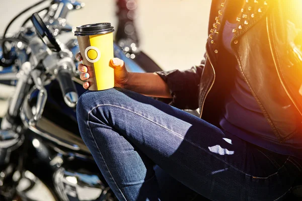 Biker girl in a leather jacket on a motorcycle drinking coffee