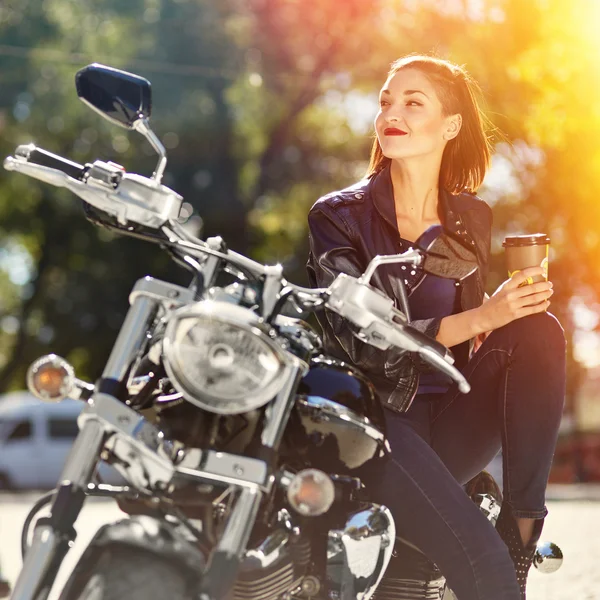 Biker meisje in een lederen jas op een motorfiets drinken koffie — Stockfoto
