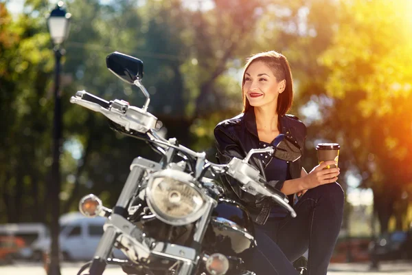 Menina motociclista em uma jaqueta de couro em uma motocicleta beber café — Fotografia de Stock