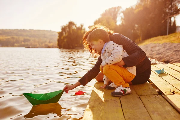 Anya és fia játszik a papír csónak a tó partján — Stock Fotó
