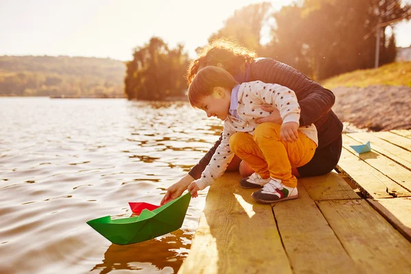 Mom and son playing with paper boats by the lake