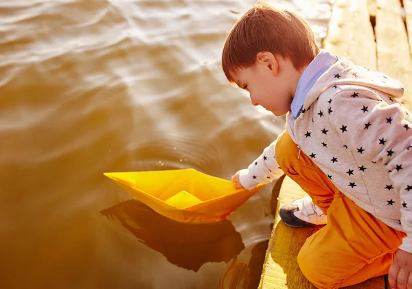 小男孩玩玩具纸船由湖 — 图库照片