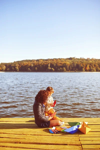 Mamá y su hijo jugando con barcos de papel junto al lago — Foto de Stock