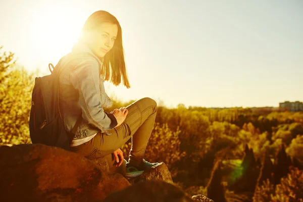 Young woman with backpack sitting on cliff — Stock Photo, Image