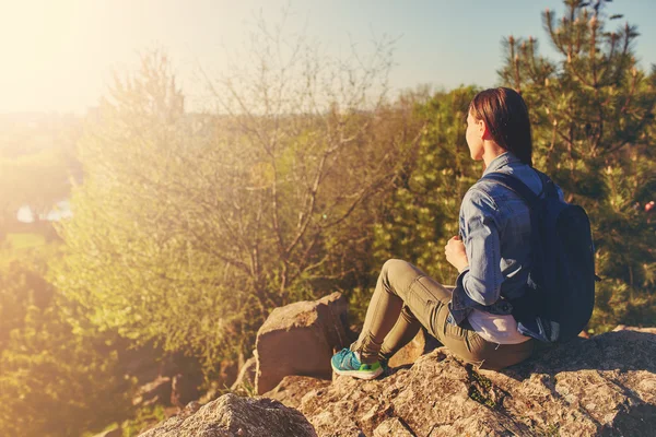 Young woman with backpack sitting on cliff — Stock Photo, Image