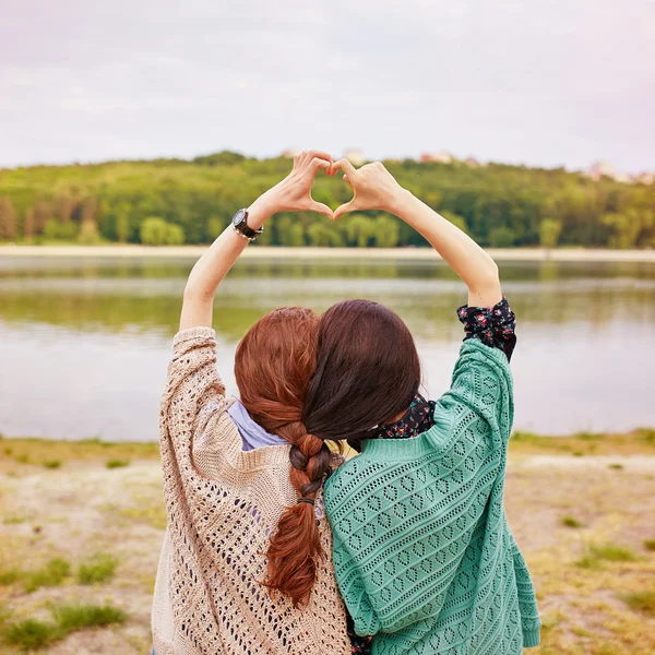 Two sisters with interwoven hairs making heart above their heads — Stock Photo, Image