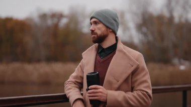 Paltolu ve bereli sakallı adam, sonbaharda nehir kenarında sıcak bir şeyler içmeyi sever..