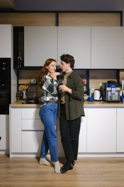 Bir çift şık bir mutfakta duruyor, şarabını yudumluyor ve hassas bir anı paylaşıyor..
