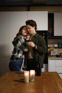 Sıcak bir mutfakta sarılıp mum ve şişenin yanında şarap içen bir çift..