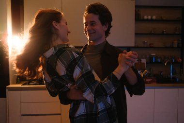 Sıcak bir mutfakta dans eden, gülümseyen ve samimi bir anda el ele tutuşan bir çift..