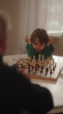 Odaklanmış genç bir çocuk, bir sonraki hamlesini dikkatlice düşünür. Yetişkin bir satranç oyununda..
