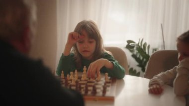 Genç bir kız düşünceli bir şekilde satranç oynuyor, aklını evinde strateji ve konsantrasyonla meşgul ediyor..