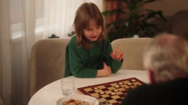 Düşünceli bir genç kız, sıcak bir evde yaşlı bir aile üyesiyle dama oynamaktan zevk alır..
