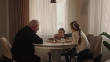 Yaşlı bir adam genç torunlarıyla düşünceli bir satranç oyunu oynar. Değerli aile anıları yaratır ve öğretme stratejisi oluşturur..