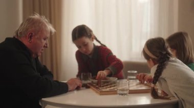 Yaşlı bir adam ve üç torunu evde bir satranç oyunu paylaşıyor, öğrenme ve aile bağlarını güçlendiriyor..