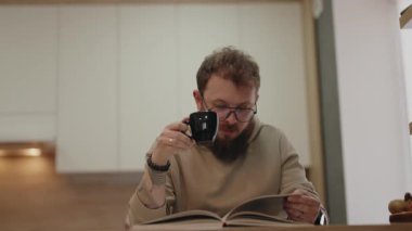 Rahat adam kitap okuyor ve modern evinde kahvesini yudumluyor..