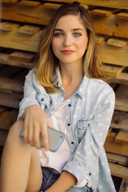 Akıllı telefon kullanarak bir palet üzerinde oturan sevimli kız