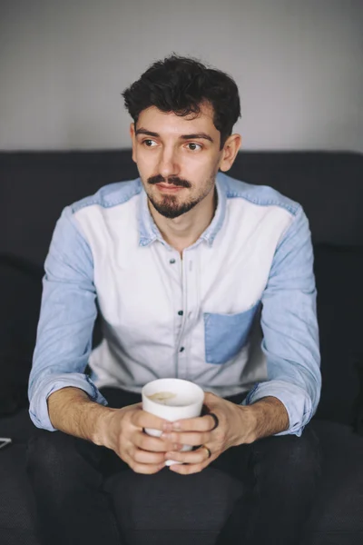 Příležitostné muž sedící na gauči s kávou — Stock fotografie