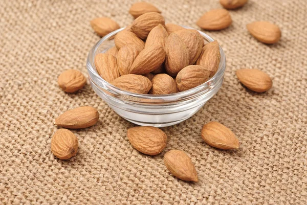 Dried almonds on glass bowl on canvas background — Stock Photo, Image