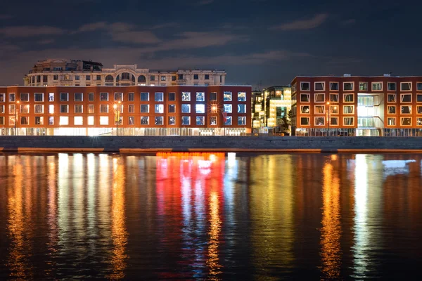 Nacht uitzicht vanaf een andere kant van de rivier van Dijk tot zakelijke gebouwen en reflectie op het water van venster licht — Stockfoto