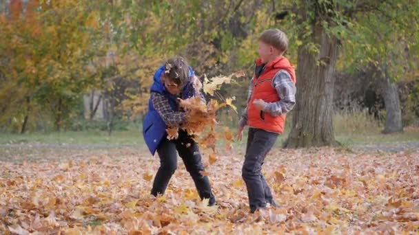 Τα αγόρια πετάνε πεσμένα φθινοπωρινά φύλλα το ένα στο άλλο. — Αρχείο Βίντεο
