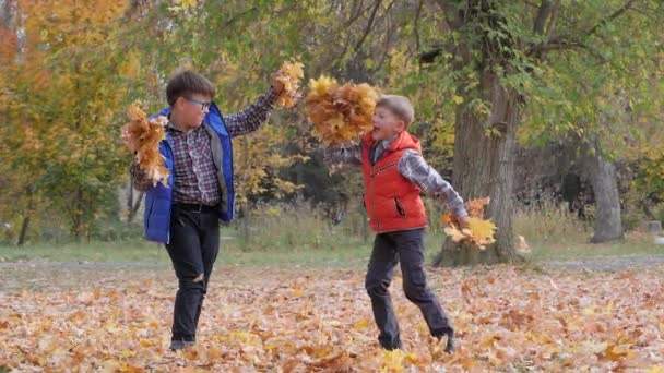 Хлопці кидають опале осіннє листя один на одного . — стокове відео