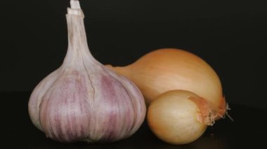Bir baş sarımsak ve siyah arka planda iki soğan..