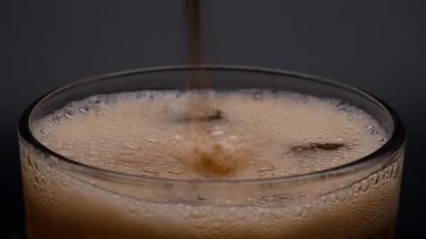 Ice glass is filled with soda water. Pouring dark carbonated drinks with ice cubes. — Stock Video