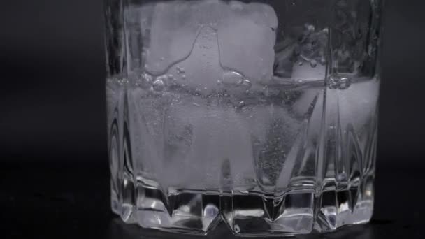 Sklenice je naplněna sodovkou. Bubliny v minerální vodě. Ledové kostky ve sklenici na černém pozadí. — Stock video