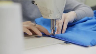Dikiş atölyesi. Endüstriyel dikiş makinesinde dikiş diken bir kadın. Eller yakın çekim. Ürüne bir fermuar ekle.