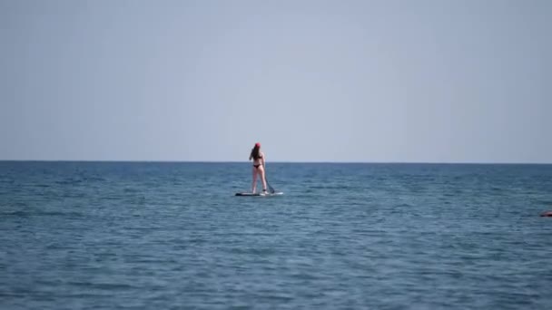 Silhouette d'un homme flottant sur une mer bleue sur une planche avec une pagaie. — Video