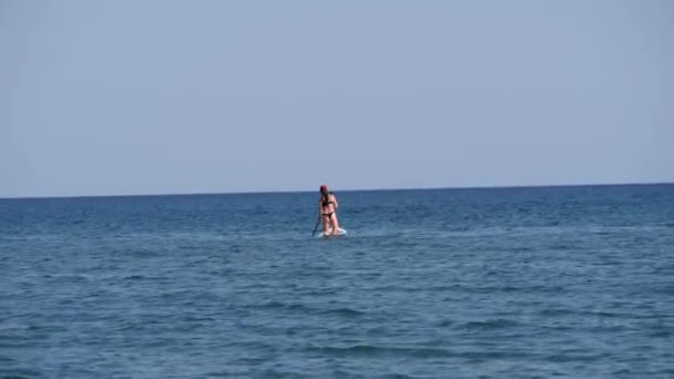 Silhouette d'un homme flottant sur une mer bleue sur une planche avec une pagaie. — Video