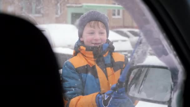 Limpieza de vidrio auto de la nieve. El niño con un cepillo libera el vidrio de la deriva de la nieve. — Vídeos de Stock