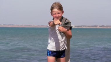 Bronz tenli, sarışın çocuk elinde havluyla bir kayanın üzerinde..