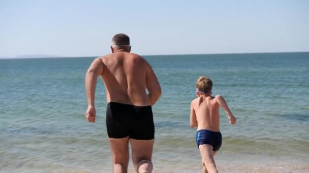 Father and son run into the blue sea. Family vacation. — Wideo stockowe