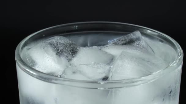 El vaso está lleno de agua de soda. Burbujas en agua mineral. Cubos de hielo en un vaso sobre un fondo negro. — Vídeo de stock