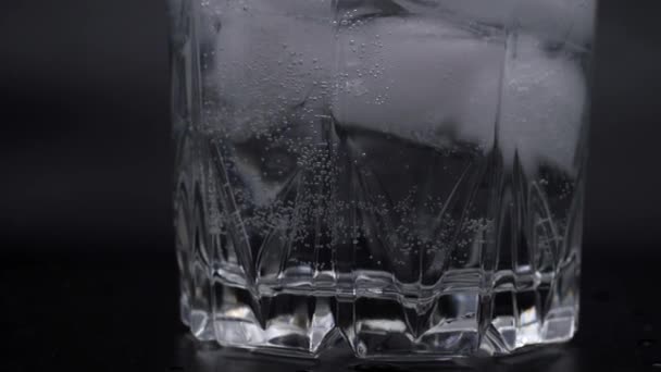 El vaso está lleno de agua de soda. Burbujas en agua mineral. Cubos de hielo en un vaso sobre un fondo negro. — Vídeo de stock