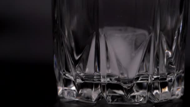 氷の塊がガラスに落ちる。黒の背景にガラスの氷のキューブ. — ストック動画
