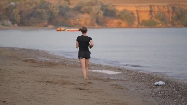 젊은 여자가해 변으로 씻겨진 모래사장에서 달리고 있다. — 비디오