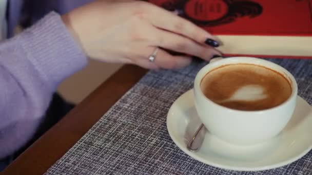 咖啡时间。女孩把书放在桌上，拿起一大杯咖啡. — 图库视频影像
