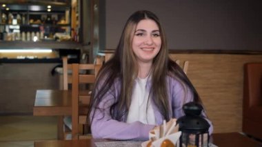 Kız gülümser, diş telleri görünür ve bardağı dudaklarına getirir..