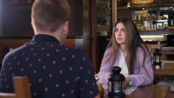 Brązowooka, długowłosa dziewczyna rozmawia z rozmówcą przy stole w kawiarni. — Wideo stockowe