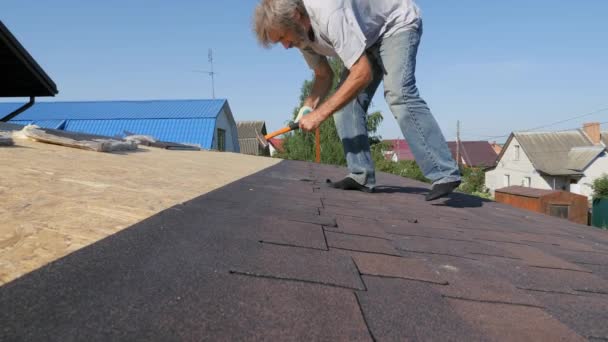 屋顶工程。用钉子和锤子钉屋顶材料。摄像机监视着安装工的工作. — 图库视频影像