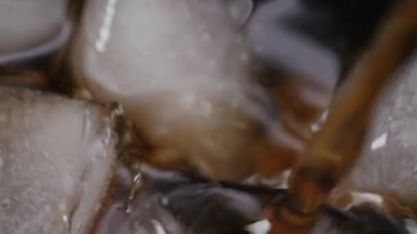 Cola gieten met ijsblokjes van dichtbij. Cola met ijs en belletjes in glas. — Stockvideo