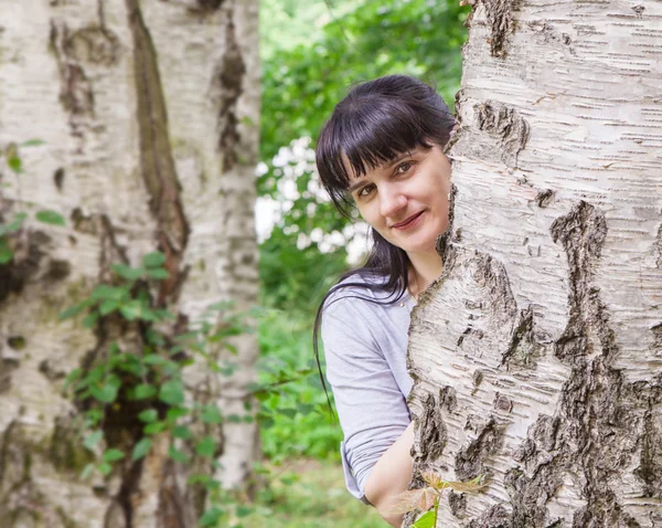 Piękna kobieta, patrząc z powodu brzozy — Zdjęcie stockowe