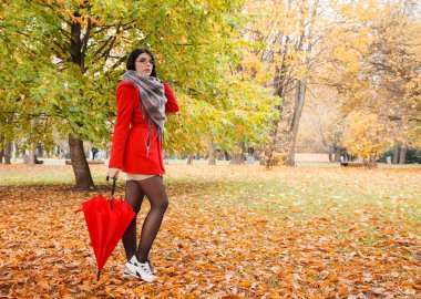 Güneşli bir sonbahar gününde şehir parkında şemsiyesi olan kırmızı ceketli genç bir kız.