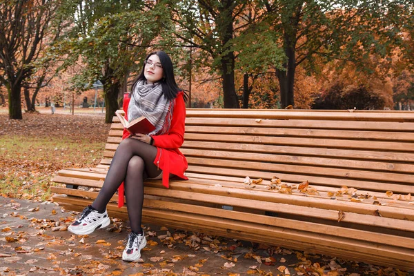Молодая Красивая Девушка Красном Пальто Читает Книгу Сидя Скамейке Парке — стоковое фото