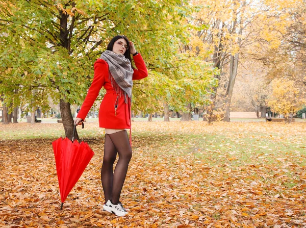 秋の晴れた日に都会の公園の路地に傘を差した赤いコートの少女 — ストック写真