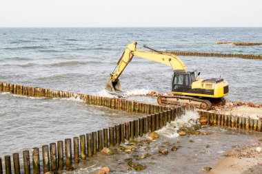 Sonbahar günü deniz kenarında bir dalgakıran inşa edilirken kazıcı