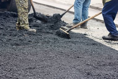 İşçiler bahar günü yol yüzeyine asfalt döşüyorlar.
